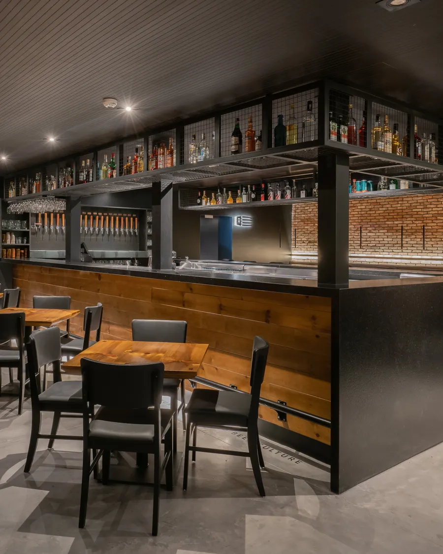 Bar do Roister Barra, com o balcão de madeira e as mesas à frente